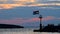 Stone pier with lighthouse and flying flag in sunset slow motion, people walking and sitting on stone wall