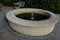 Stone sandstone circular fountain in the park. built of sandstone filled with water. lined with a light threshing gravel road with