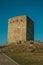 Stone square tower over rocky hill on sunset