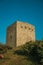 Stone square tower over rocky hill on sunset