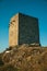 Stone square tower over rocky hill on sunset