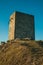 Stone square tower over rocky hill on sunset