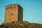 Stone square tower over rocky hill on sunset