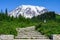 Stone stairs leaning to a gravel hiking path with a person walking up the trail towards Mt Rainier, snow and glacier covered peak