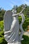 Stone statue of an angel, a girl on a stone with a dove in hand against a background of a pine forest and a blue sky