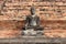 A stone statue of Buddha was installed in front of a brick wall in a park in Sukhothai (Thailand)