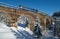 Stone viaduct arch bridge on railway through mountain snowy fir forest and locomotive  with a passenger train. Snow drifts  on