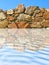 Stone wall being reflected in ripple blue water.