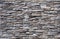 Stone wall made of striped stacked embossed natural rocks. Colors are gray, black, brown and white.