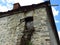 A stone wall of an old abandoned ruined house, window, chimney and house roof.