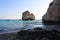 Stones on the beach of Aphrodite and the legendary Aphrodite`s Rock on the background of blue cloudless sky. Cyprus