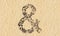Stones on beach sand handmade symbol shape, golden sandy background, sign of ampersand
