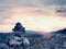 Stones pyramid on Alpine gravel mountain summit. Daybreak horizon above blue mist in valley.