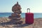 Stones stacked on a pile and red suitcase on a sea shore at Mediterranean sea.