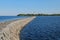 Stony breakwater dam quay and lighthouse on the Ladoga lake. Sunny summer landscape. Blue sky reflects in water surface