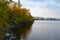 On a stony shore, trees with colorful autumn leaves bend over calm water