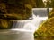 Stony weir on small mountain river. Stream is flowing over blocks and makes milky water.