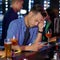 Stood up again. Shot of an upset looking young man reading a text on his cellphone while sitting at the counter of a