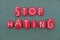 Stop Hating slogan composed with red colored stone letters over green sand