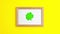 Stop motion animation of green paper clovers on wooden frame at the left with white copy space on yellow background Saint Patrick