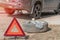 Stop sign in front of the car. Replacing the wheel on the road by the driver. Replacement of tires on the car by a