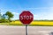 A stop sign in front of a rapeseed field and a blue sky.