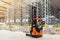 Storehouse employee in uniform working on forklift in modern automatic warehouse. Boxes are on the shelves of the warehouse.