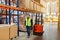 Storehouse employee in uniform working on forklift in modern automatic warehouse. Boxes are on the shelves of the warehouse.