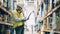 Storeman in uniform typing on laptop among warehouse shelves