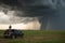 storm chaser observes powerful tornado from a safe distance, with storm clouds spinning in the background