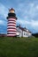 Storm Clouds Gather Around Red and White Striped Lighthouse in New England