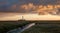 Storm clouds at sunset over the lighthouse of Westerhever. In the foreground a small channel leads into the picture