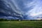 Storm dark clouds flying over field with green grass