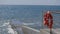 Storm at sea, big waves crashing on the concrete pier. On the fence hangs a lifeline.