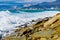 Storm waves in white foam break on the beach, strewn with fragments of yellowish Sandstone rocks.