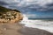 Stormy coastline with water splash and dark sky, sandy beach with turquoise sea, Sitges, Spain