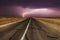 Stormy country road at night, with intense lightning strikes.