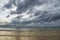 Stormy dark clouds above the sea with sandy beach and curling waves