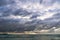 Stormy dark clouds above the sea with sandy beach and curling waves