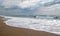 Stormy sea waves breaks about empty beach under cloudy sky