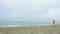 Stormy seaside, gray clouds on horizon. Young brunette female running on beach