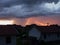 Stormy severe weather with dark clouds, cloudburst or shower and sunshine behind rain above settlement during summer evening