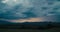 Stormy sky on countryside with mountain and rain on horizon in timelapse