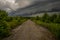 Stormy sky, low thunderclouds hanging over the dirt road leading into the forest
