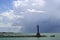 Stormy sky over ocean with a breakwater made of bags of concrete stretching out with a rustic lighthouse at the end and birds