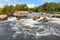 Stormy streams of water wash over the rocky banks of the river, overcoming rapids on a bright summer day