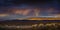 Stormy Sunset with rain and rainbow in the desert with light on mountain range.