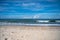 Stormy surf on the seashore, with white foam on the yellow sand. Skyline over the sea with blue sky and cumulus clouds