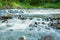 A stormy, turbulent river with a strong current. Streams of water wash large stones in the river. Clear water in a mountain river