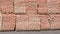 Stowed on top of each other are two rows of wooden pallets, standing with stacks of red bricks stacked on them in several levels